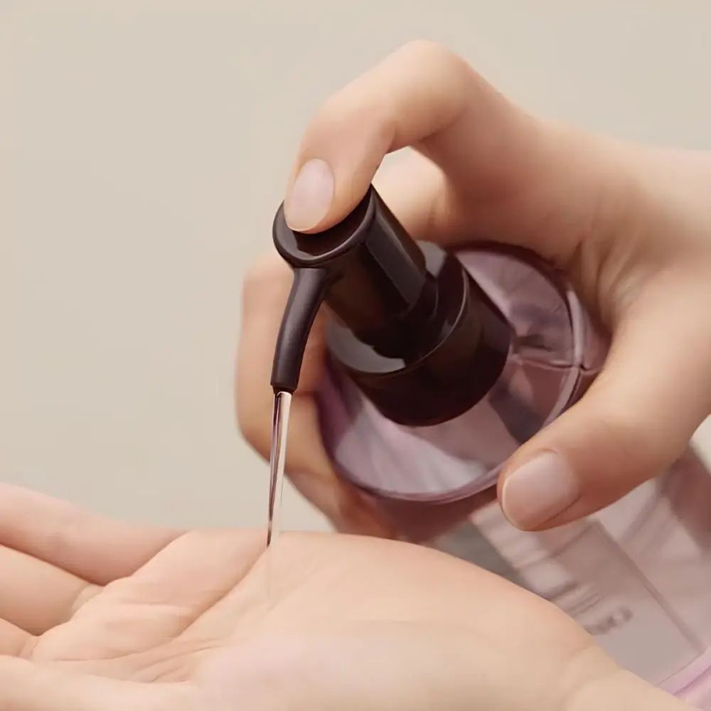 Mano che eroga olio da un flacone. Goccia di olio nel palmo. Flacone "FIG CLEANSING OIL".