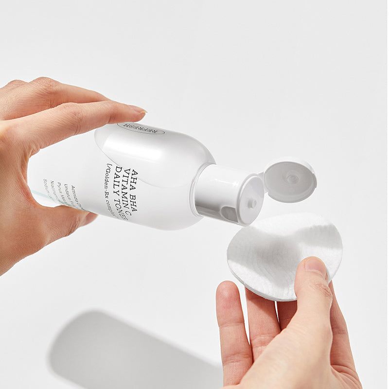 Mani che tengono un flacone e un batuffolo di cotone. Flacone con scritta: AHA BHA Vitamin C Daily Toner.