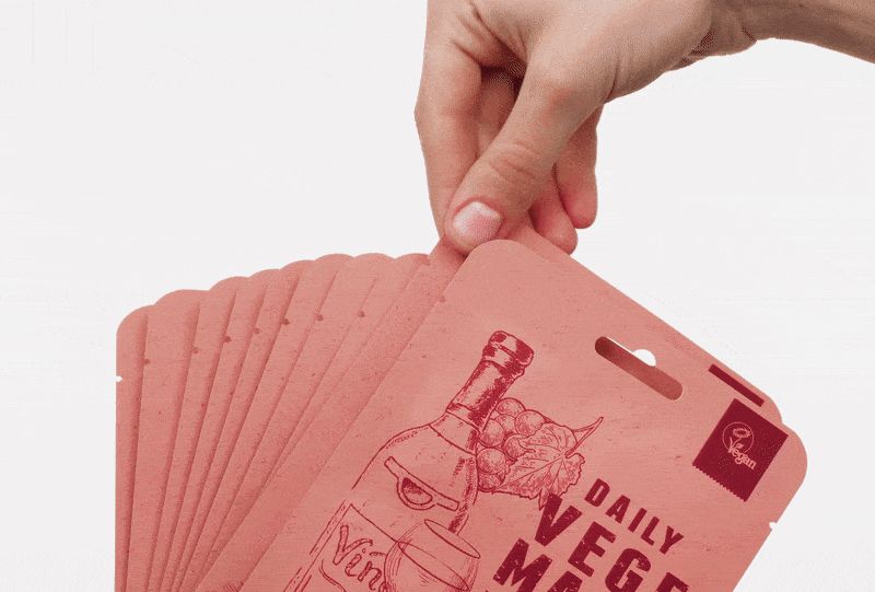 Mano che tiene diverse confezioni di maschere rosa. Stampa: DAILY VEGE MASK, illustrazione del vino. Confezioni con foro per appendere.