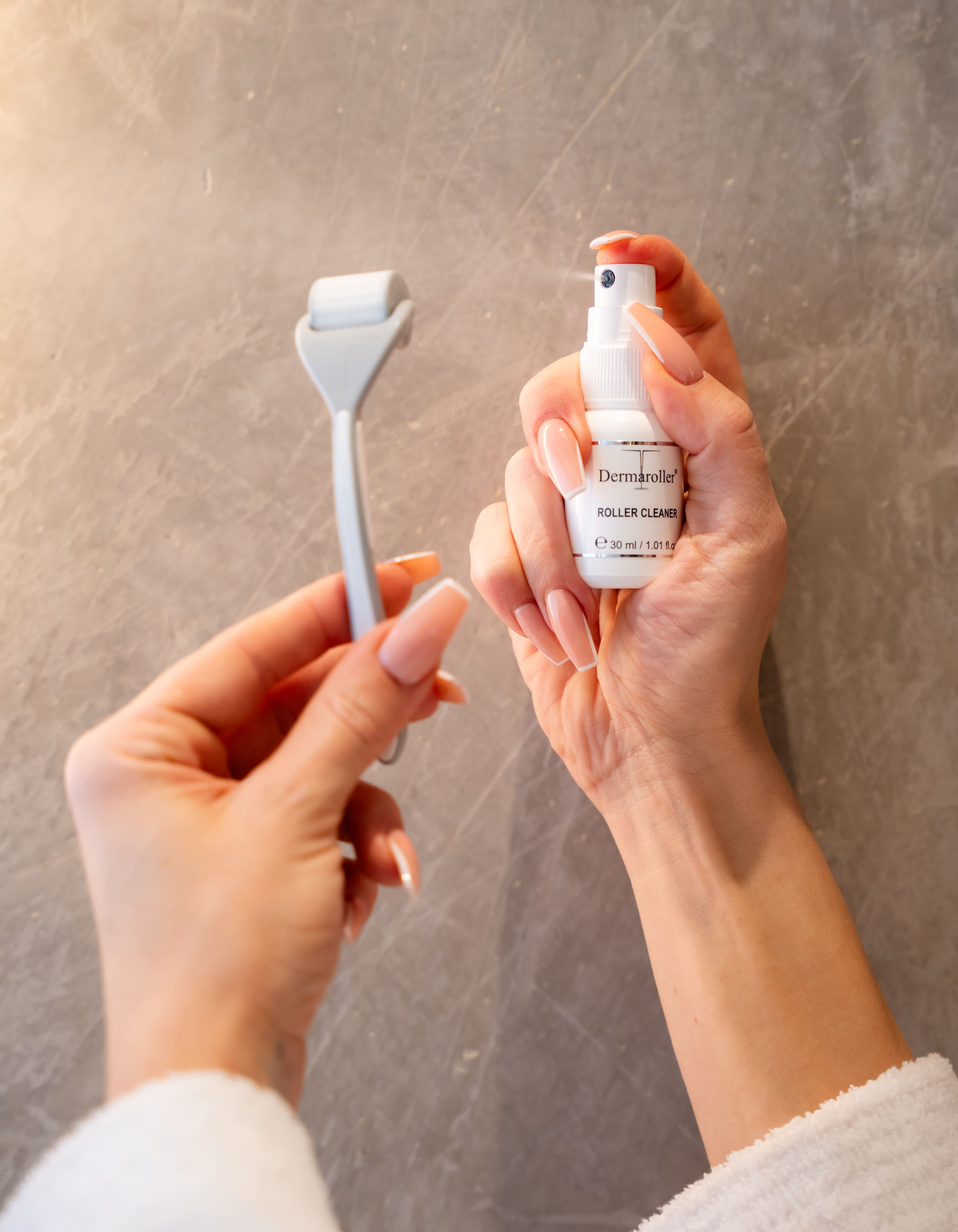 Mani che tengono Dermaroller e Roller Cleaner. Flacone spray con la scritta "Roller Cleaner".