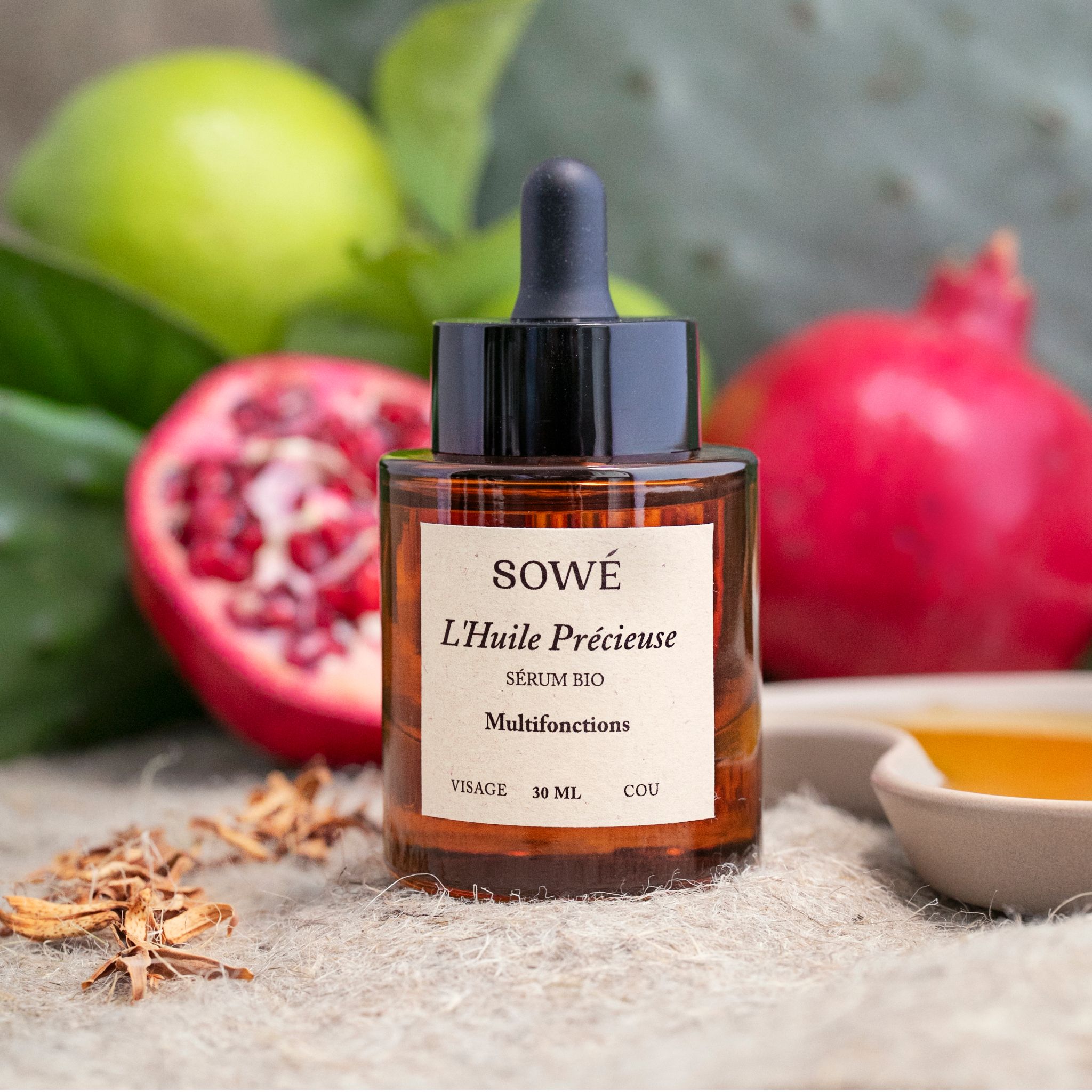 Flacone di vetro marrone con pipetta. Etichetta con nome e testo del prodotto. Melograno e lime sullo sfondo.