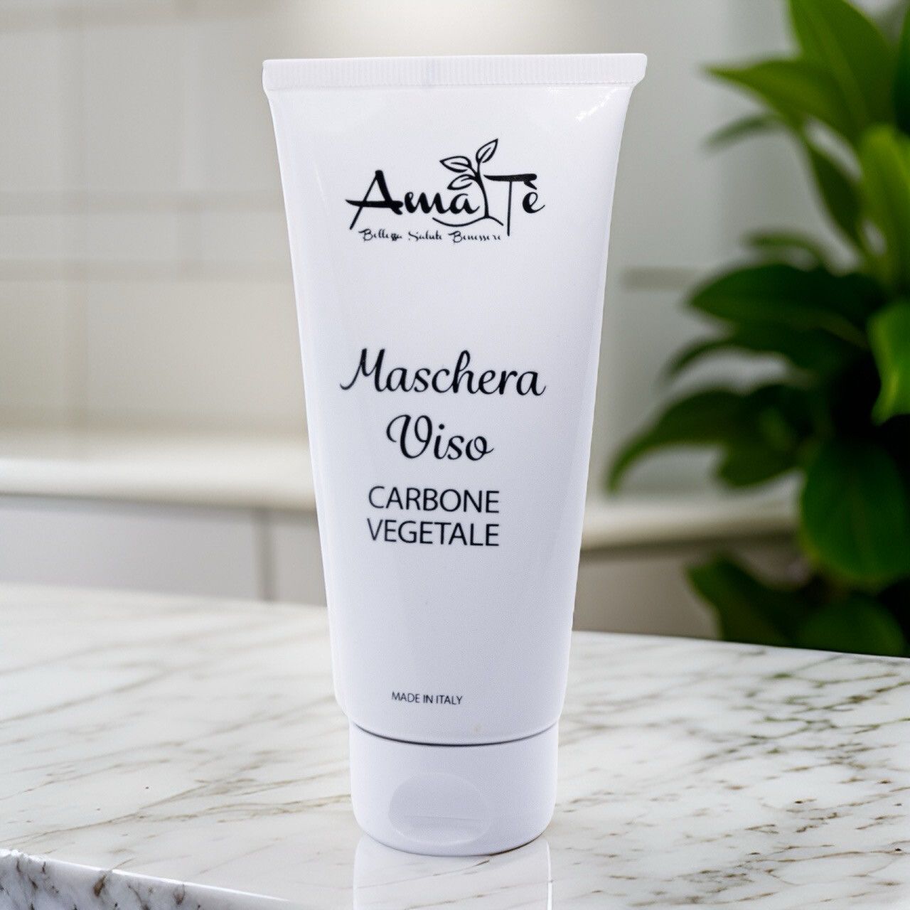 Tubo bianco Amatè Maschera Viso Carbone Vegetale su superficie bianca. Pianta sullo sfondo.