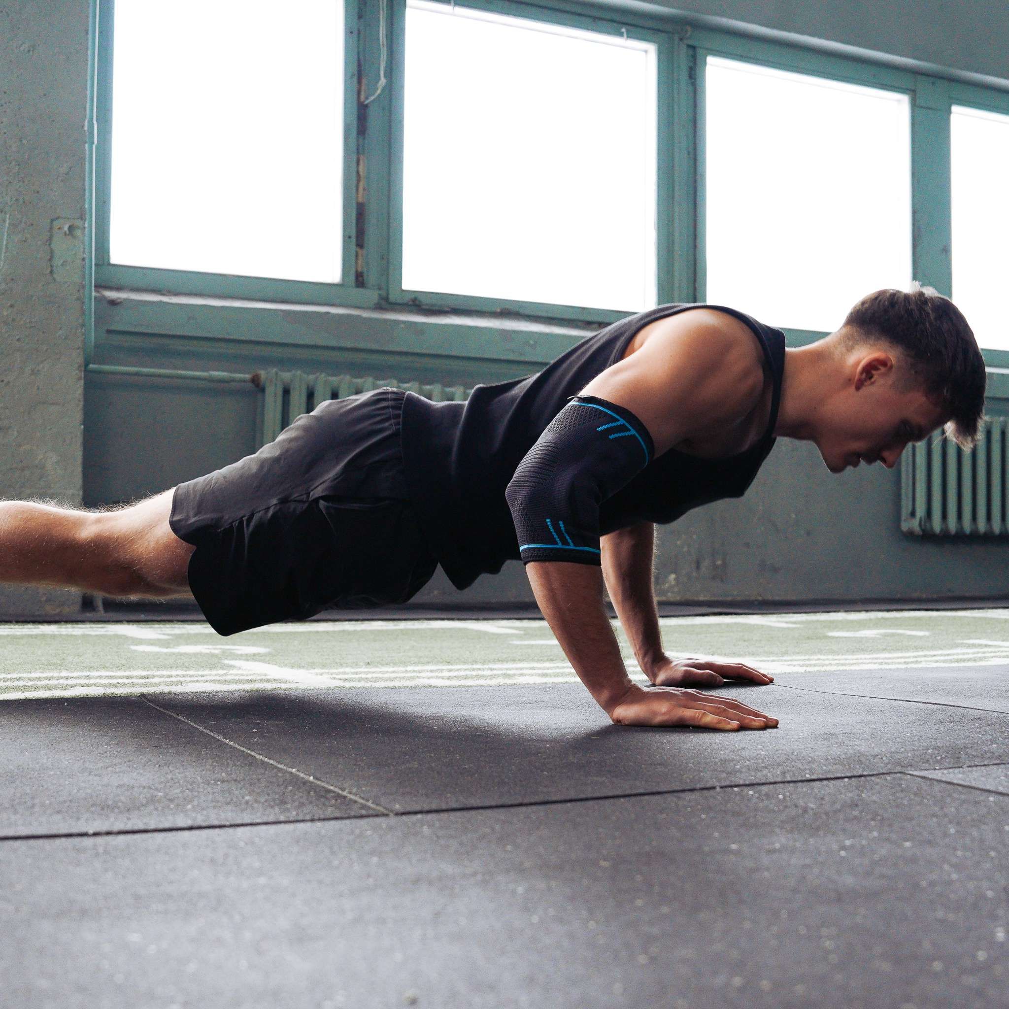 Uomo in palestra che fa flessioni. Indossa un tutore per gomito nero con dettagli blu.