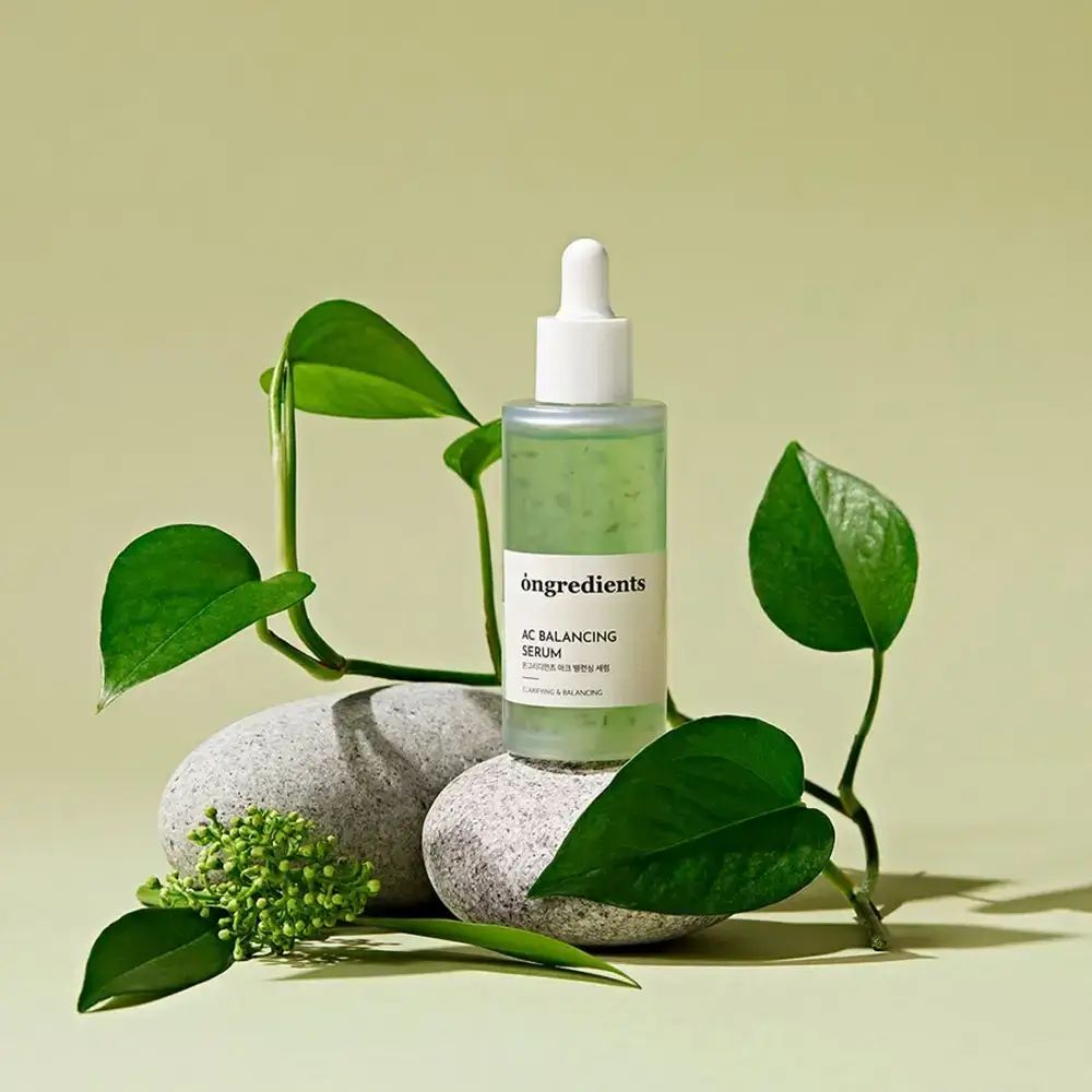 Siero verde in bottiglia di vetro con pipetta. Posizionato su pietre e foglie. Nome prodotto: Ongredients AC Balancing Serum.