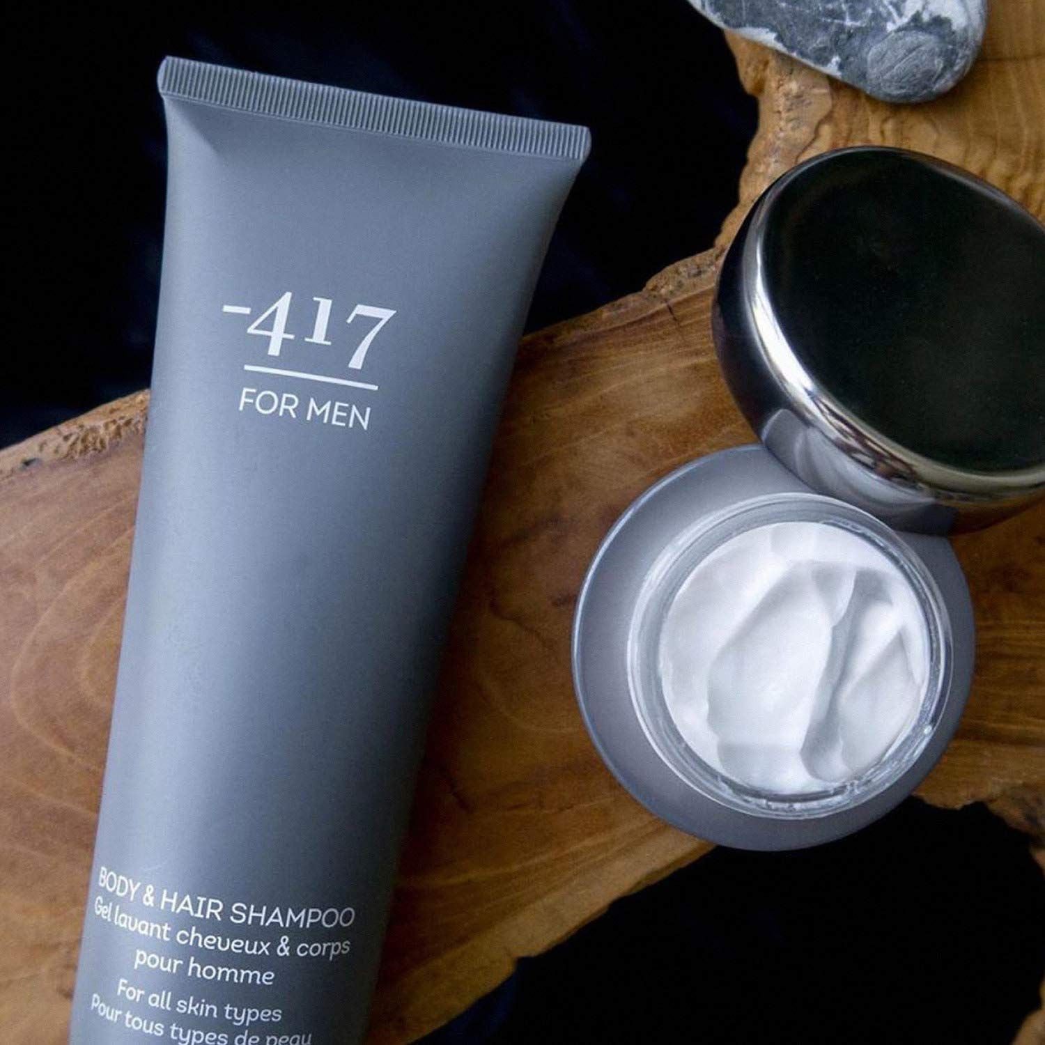 Tubo di shampoo grigio accanto a un vasetto di crema e pietre su legno. Testo: -417 FOR MEN, Body & Hair Shampoo.