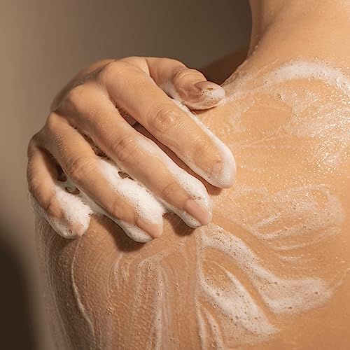 Primo piano di una persona che applica sapone sulla spalla. La schiuma copre la pelle.