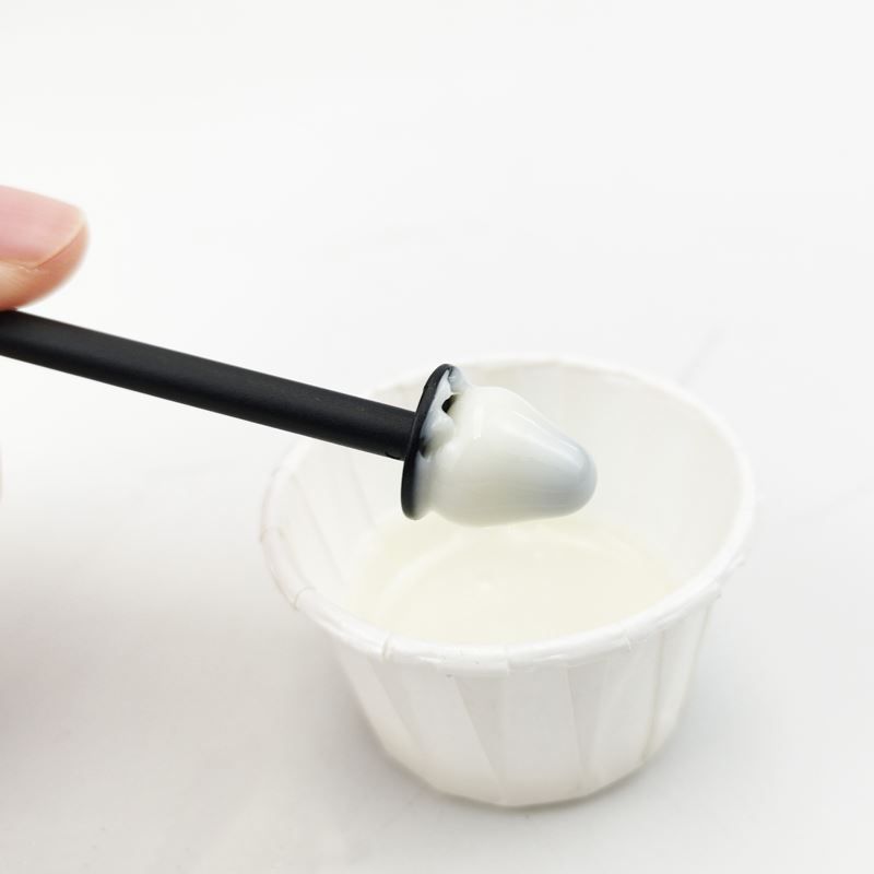 Un applicatore con cera bianca viene immerso in una piccola coppetta di carta con cera liquida.