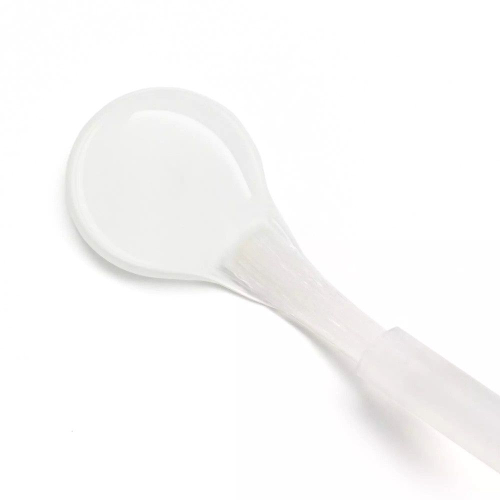 Primo piano del pennello di un esfoliante per cuticole. Il pennello è bianco e di forma ovale.