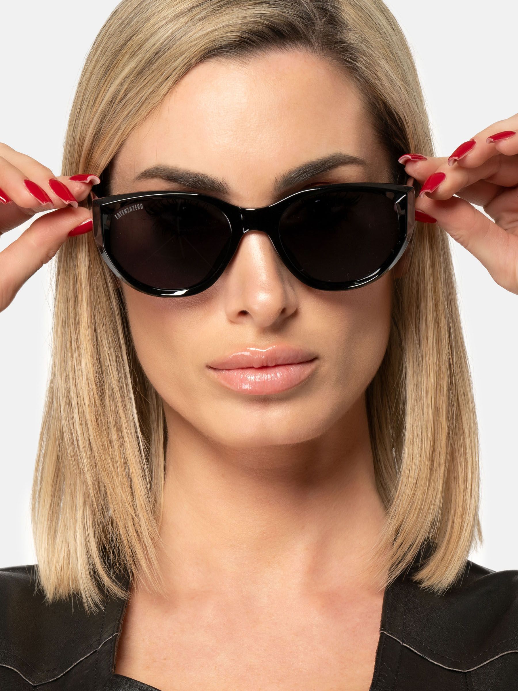 Donna con occhiali da sole neri. Tiene gli occhiali con le mani.