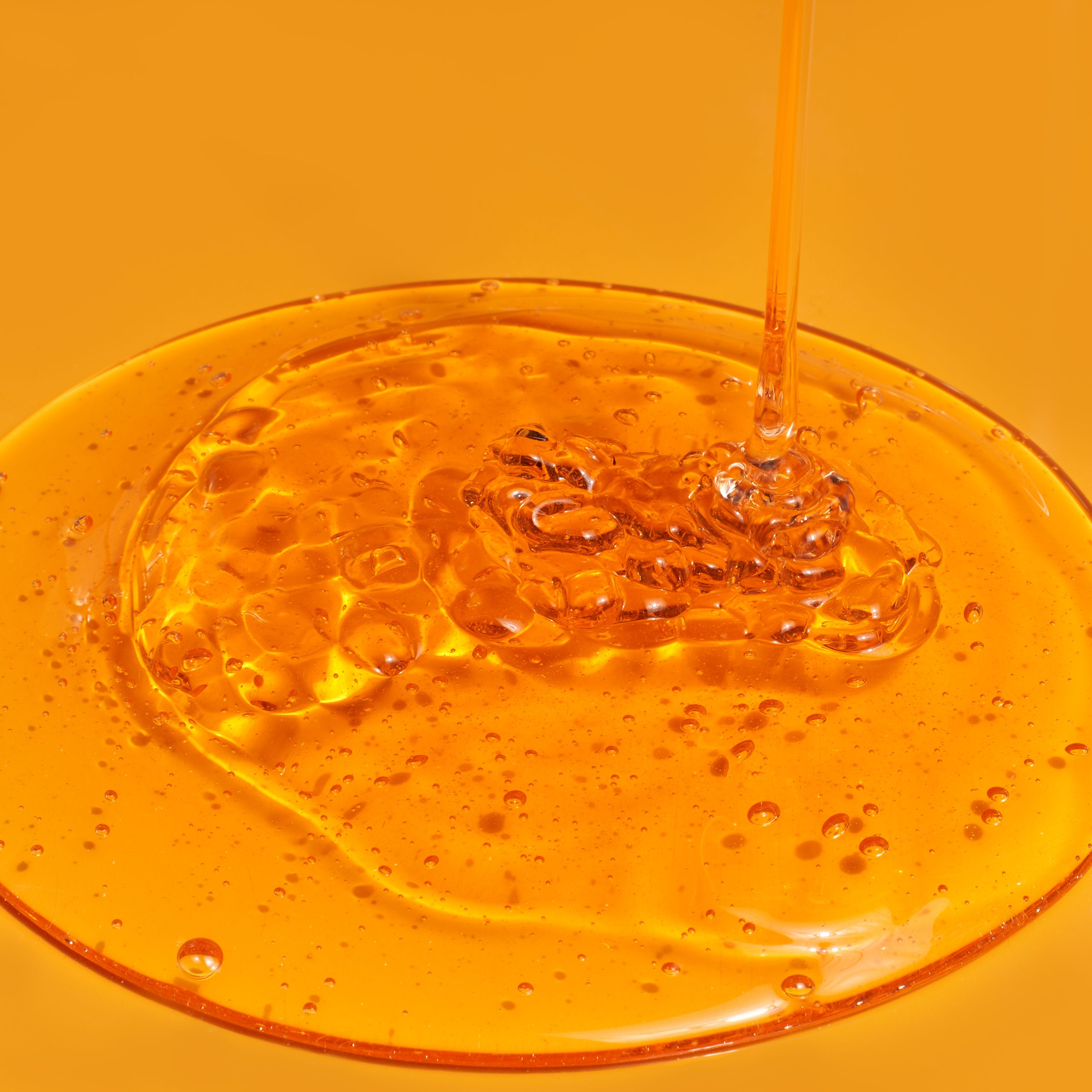 Liquido ambrato versato su una superficie. Presenza di bolle. Primo piano.