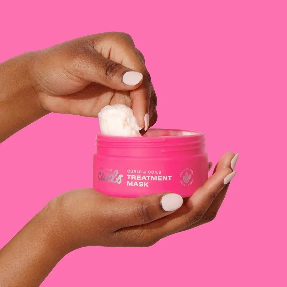 Vasetto rosa di maschera per ricci. Mani che tengono il vasetto e prelevano il prodotto. Sfondo rosa.