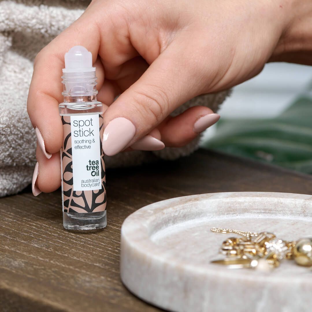 Flacone roll-on con testo: Spot Stick, Tea Tree Oil, Australian Bodycare. Su un vassoio vicino a gioielli.