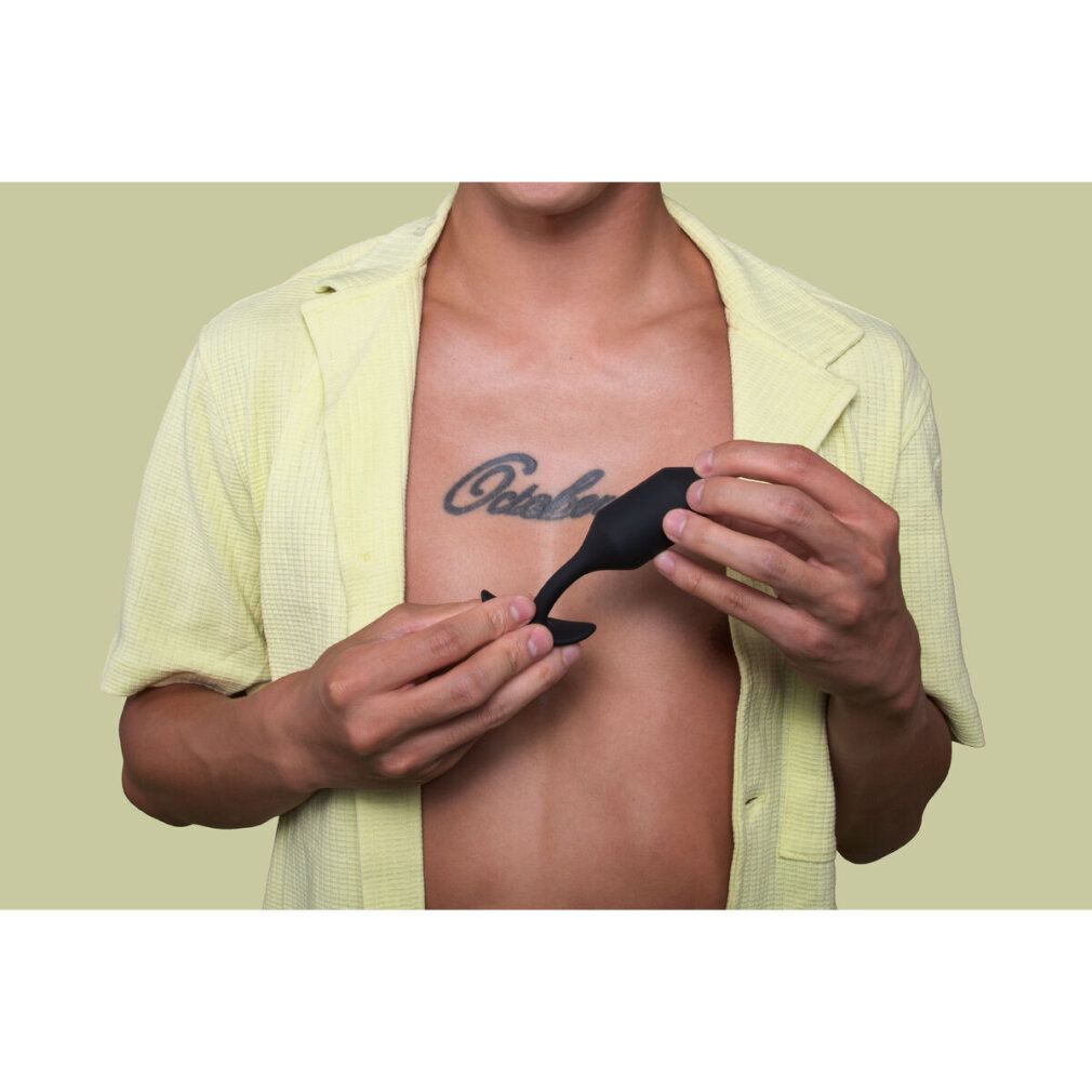 Persona che tiene un plug nero. Petto con tatuaggio. Camicia gialla.