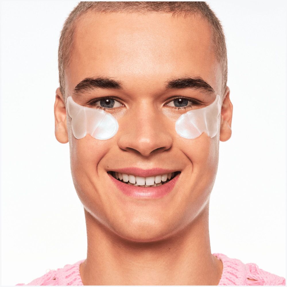 Uomo con patch per occhi. Patch bianchi sulla pelle sotto gli occhi. Sorride alla fotocamera.