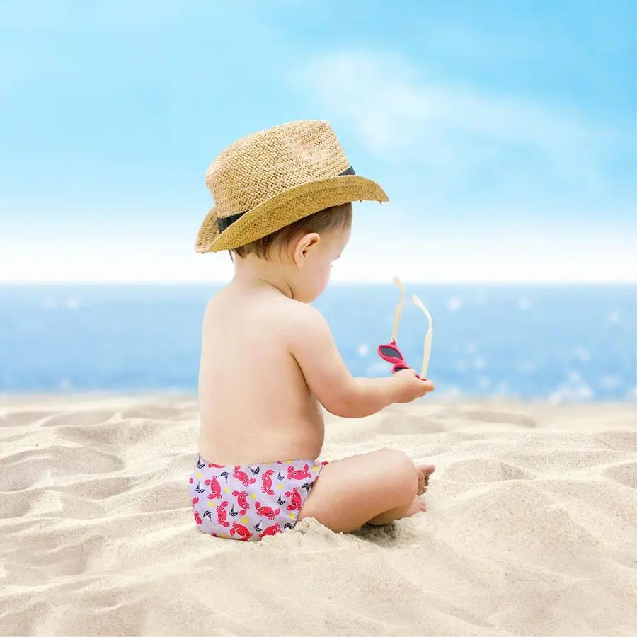 Bambino sulla spiaggia, indossa costumino con motivo a granchio. Con cappello e occhiali da sole.