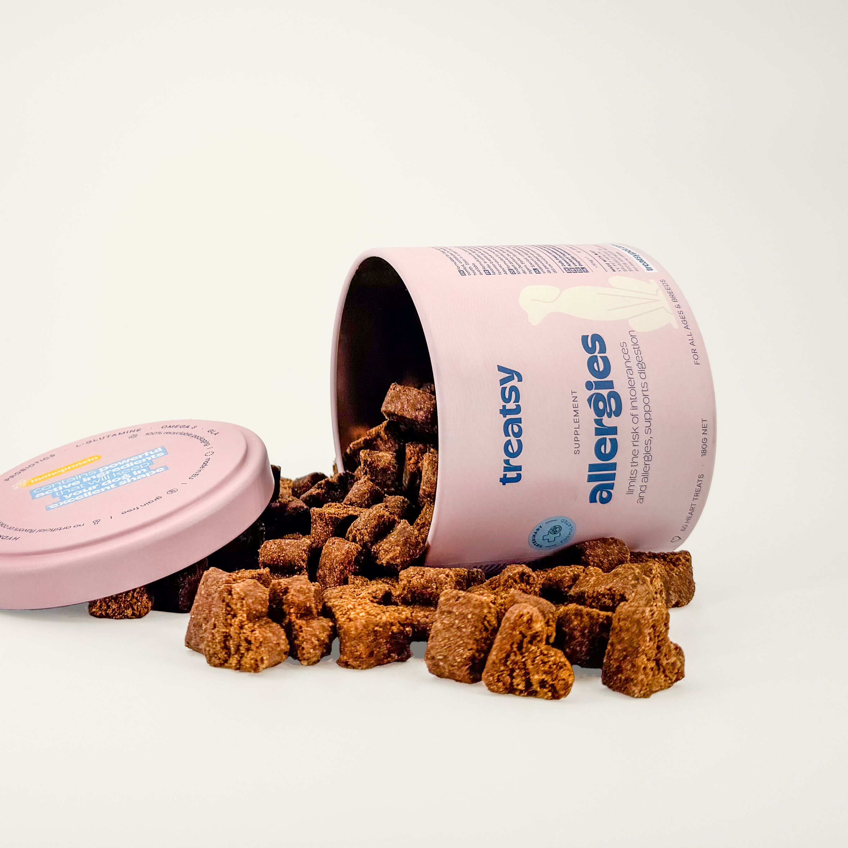 Barattolo rosa con "Treatsy Allergies" per cani, rovesciato. Snack a forma di cuore accanto.