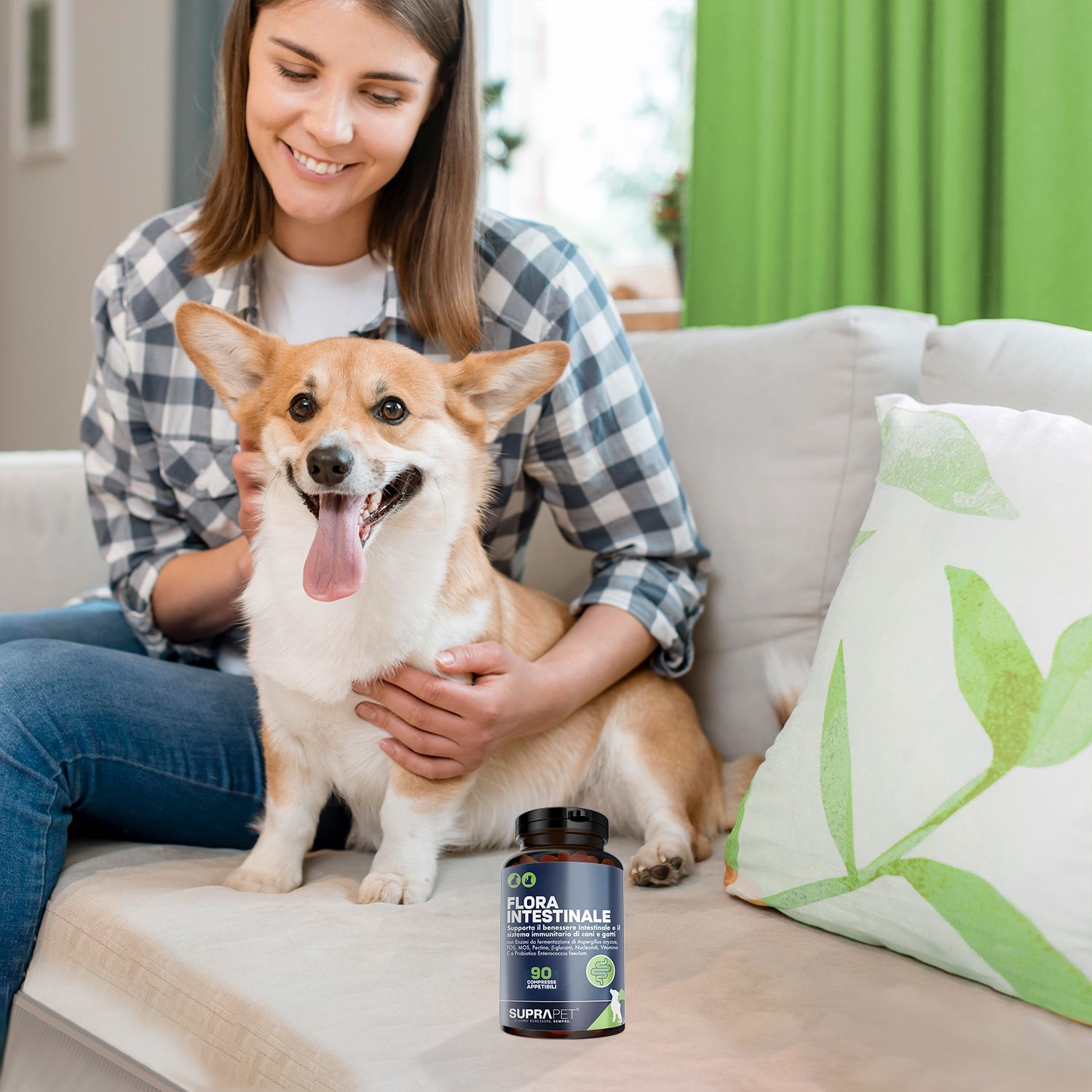 Una donna accarezza un Corgi su un divano. Accanto c'è una bottiglia di integratori alimentari.
