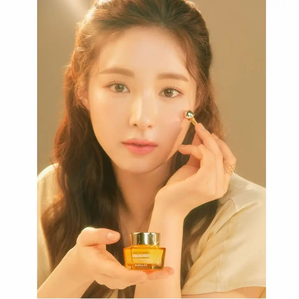 Donna che tiene un vasetto dorato e un applicatore. Scritta: Miss Flower & Mr. Honey. Tocca il suo occhio con l'applicatore.