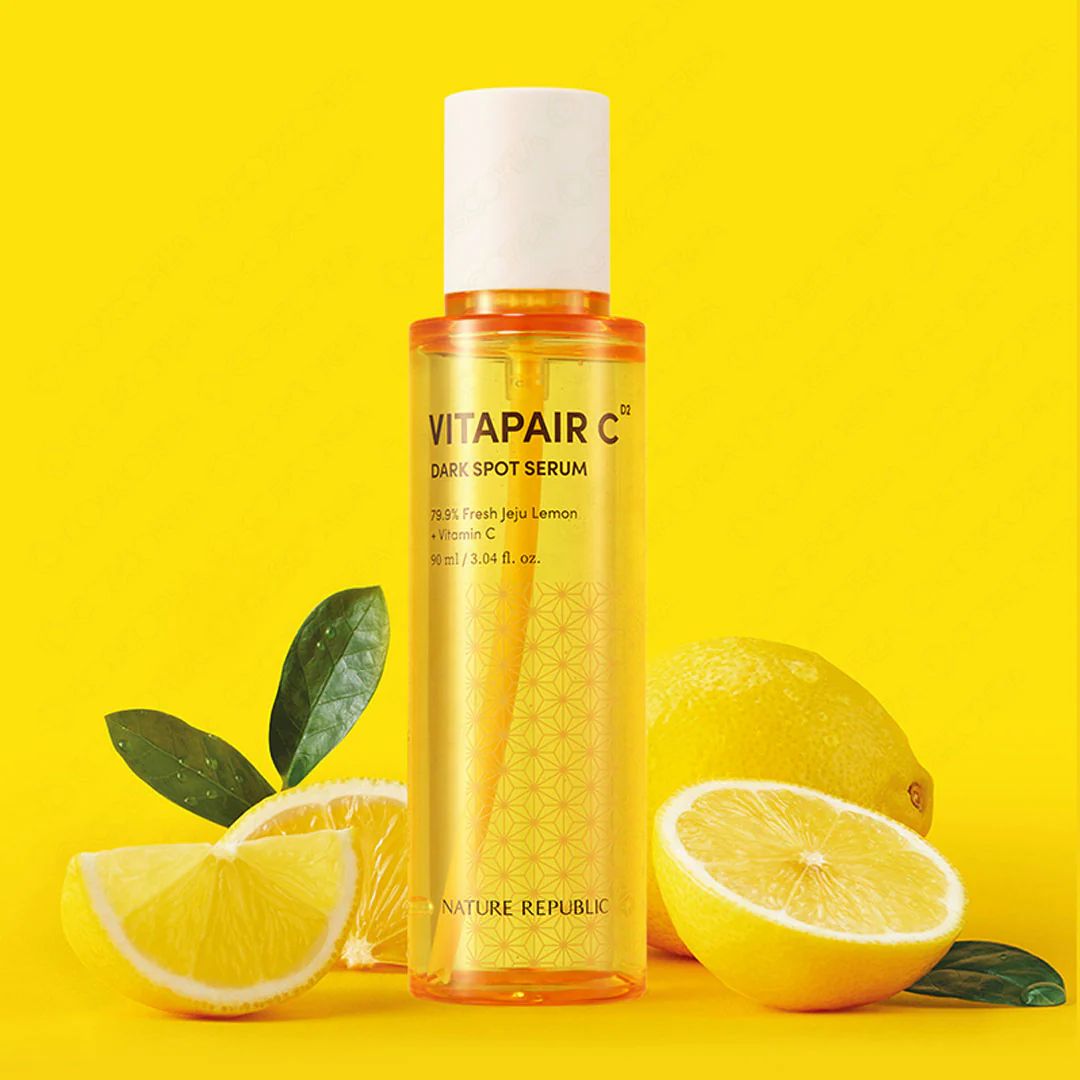 Flacone di siero con tappo bianco, liquido giallo e nome del prodotto. Limoni e foglie accanto.