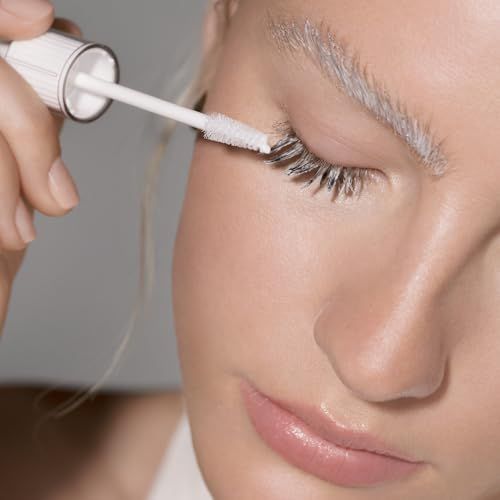 Primo piano di una donna che applica un prodotto bianco sulle ciglia con un applicatore.