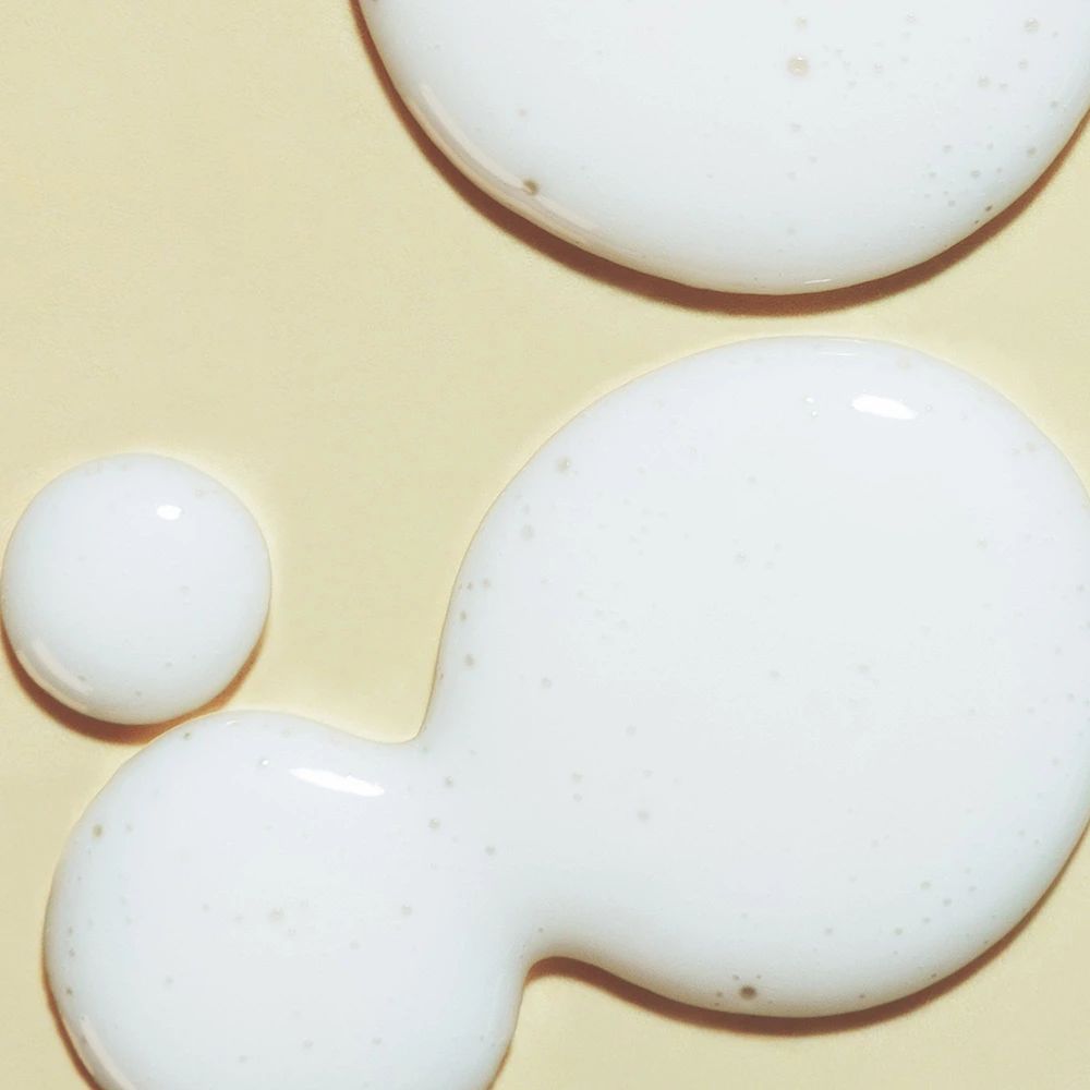 Primo piano di gocce bianche di liquido su sfondo giallo. Alcune gocce sono più grandi di altre.