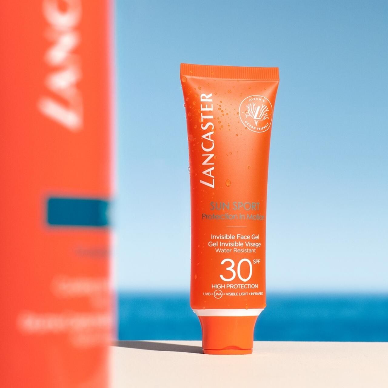 Tubo arancione Lancaster Sun Sport Invisible Face Gel SPF30. Davanti cielo blu.