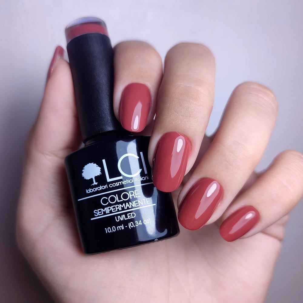 Mano che tiene un flacone di smalto e unghie smaltate. LCI Cosmetics, smalto semipermanente, colore Rosso. Flacone nero.