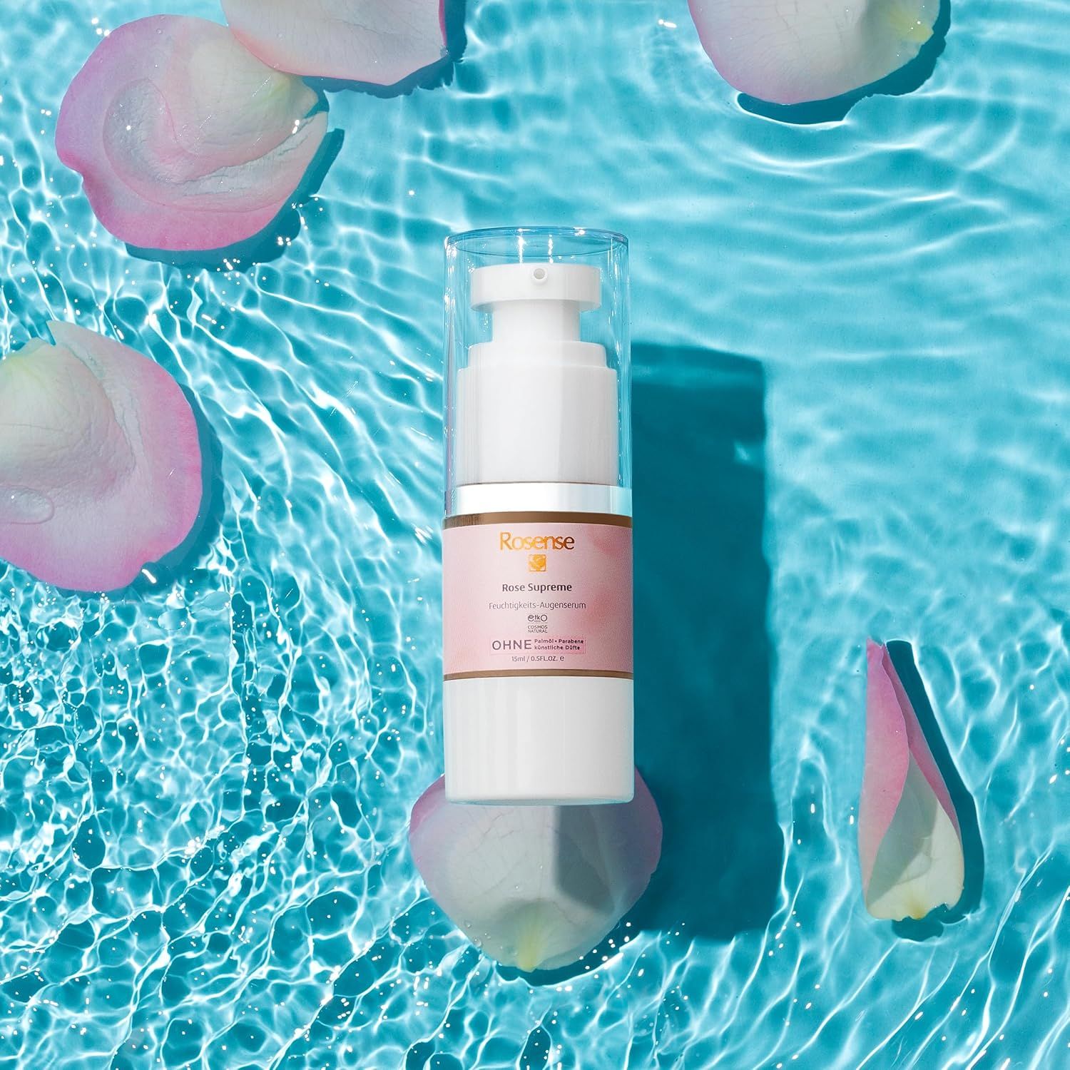 Dispenser bianco Rosense Supreme Augenserum su acqua blu con petali. Coperchio trasparente, etichetta rosa, testo.