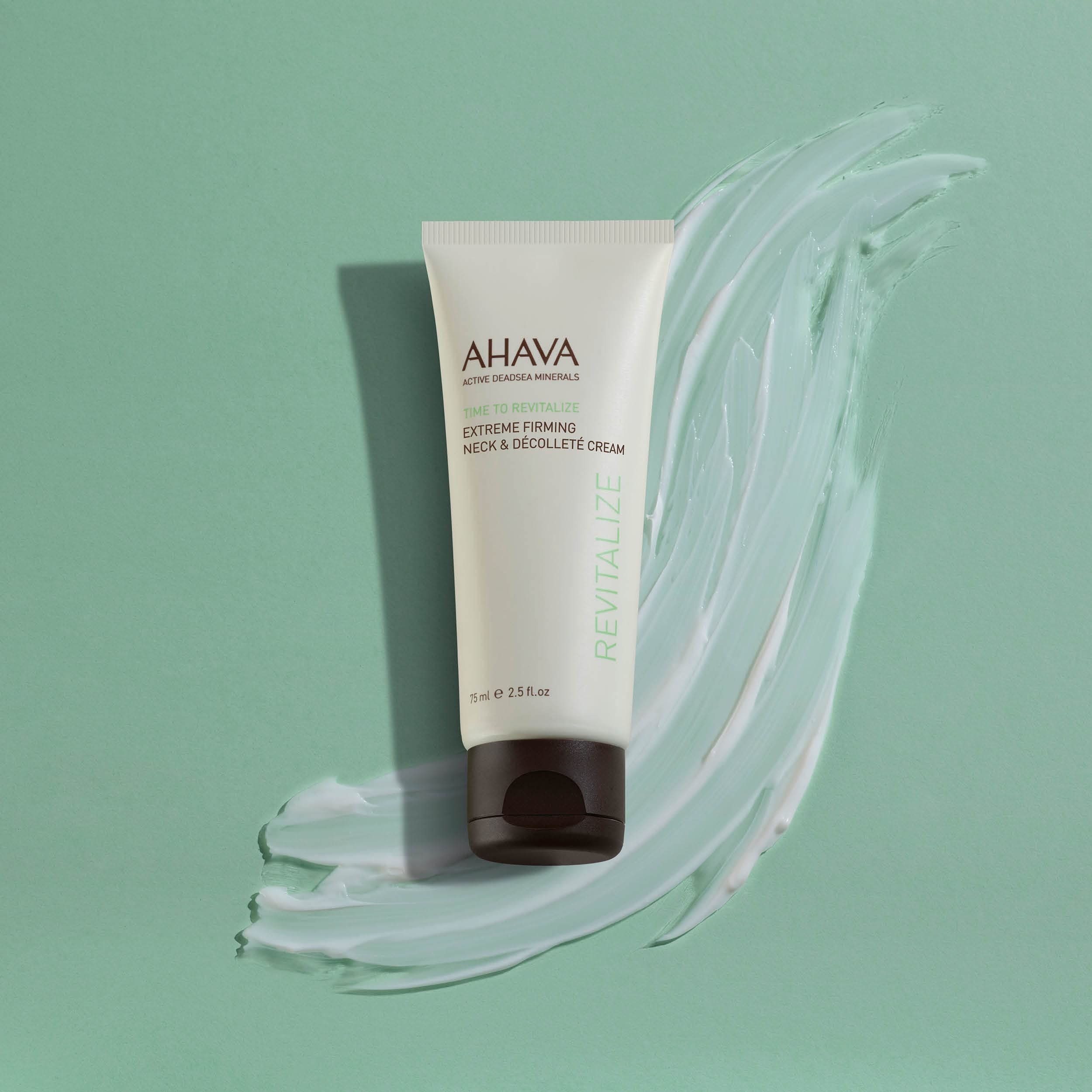 Tubo di crema davanti a uno sfondo con un campione di crema. Tubo con nome e descrizione del prodotto. Testo: AHAVA, Time To Revitalize, Extreme Firming Neck & Décolleté Cream.
