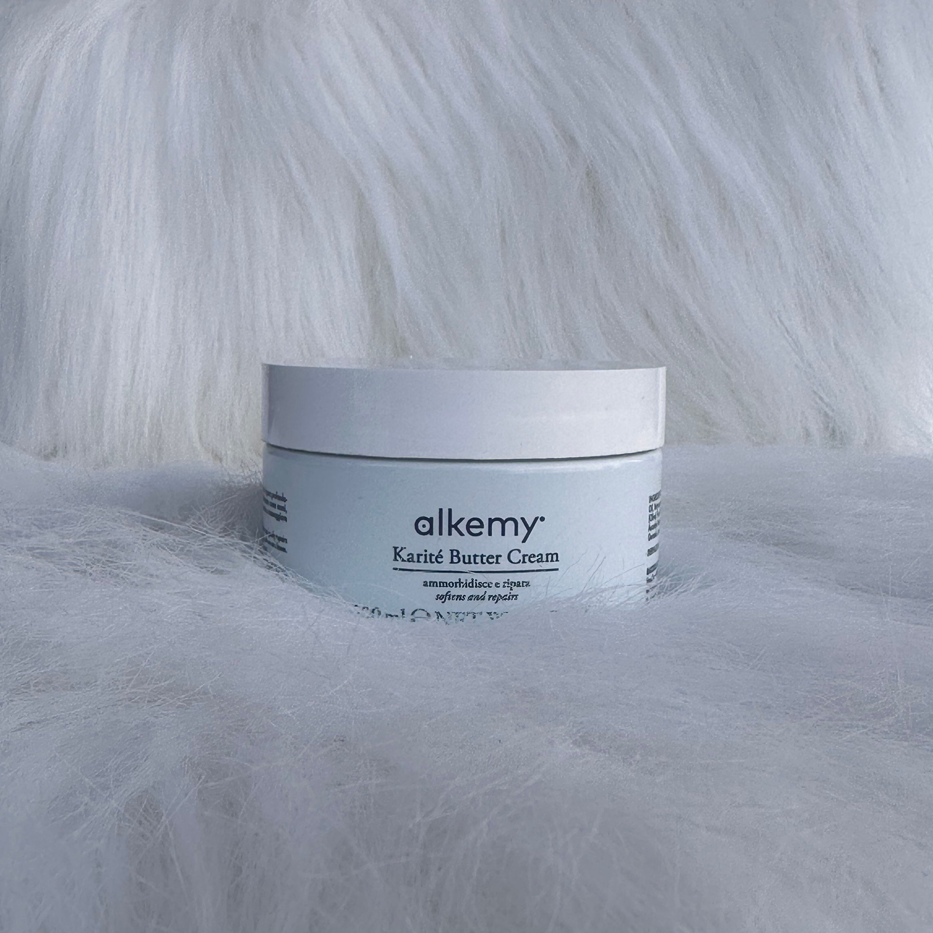 Un contenitore bianco con etichetta 'alkemy Karité Butter Cream' su sfondo soffice.