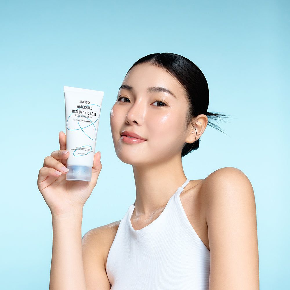 Una donna tiene in mano un tubo di schiuma detergente. Sul tubo: JUMISO Waterfull Hyaluronic Acid Cleansing Foam.