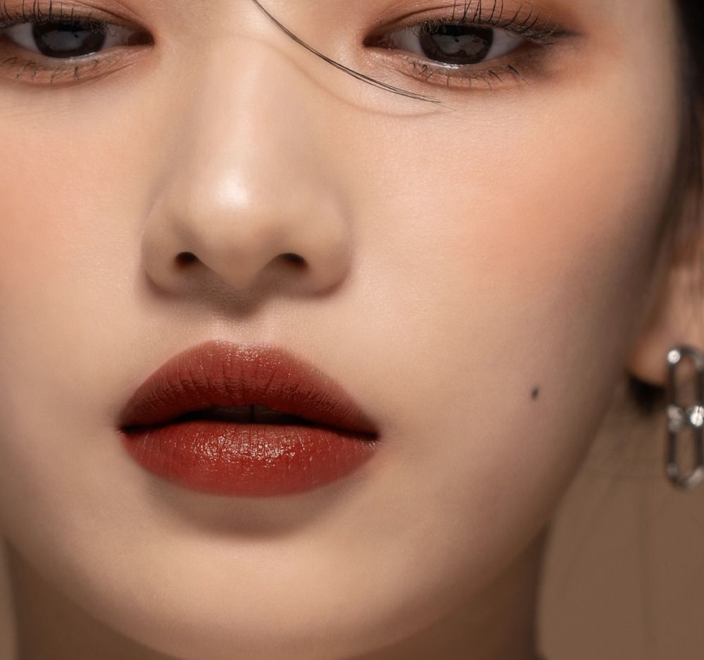 Primo piano di un viso con labbra coperte di lucidalabbra. Colore scuro e lucido. Occhi visibili.