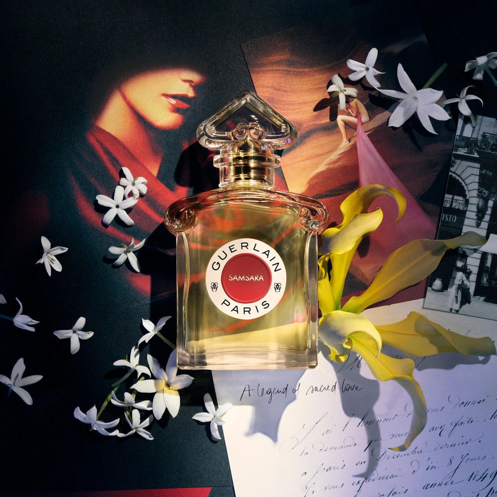 Flacone di profumo Samsara Paris con etichetta rossa, circondato da fiori e elementi decorativi.