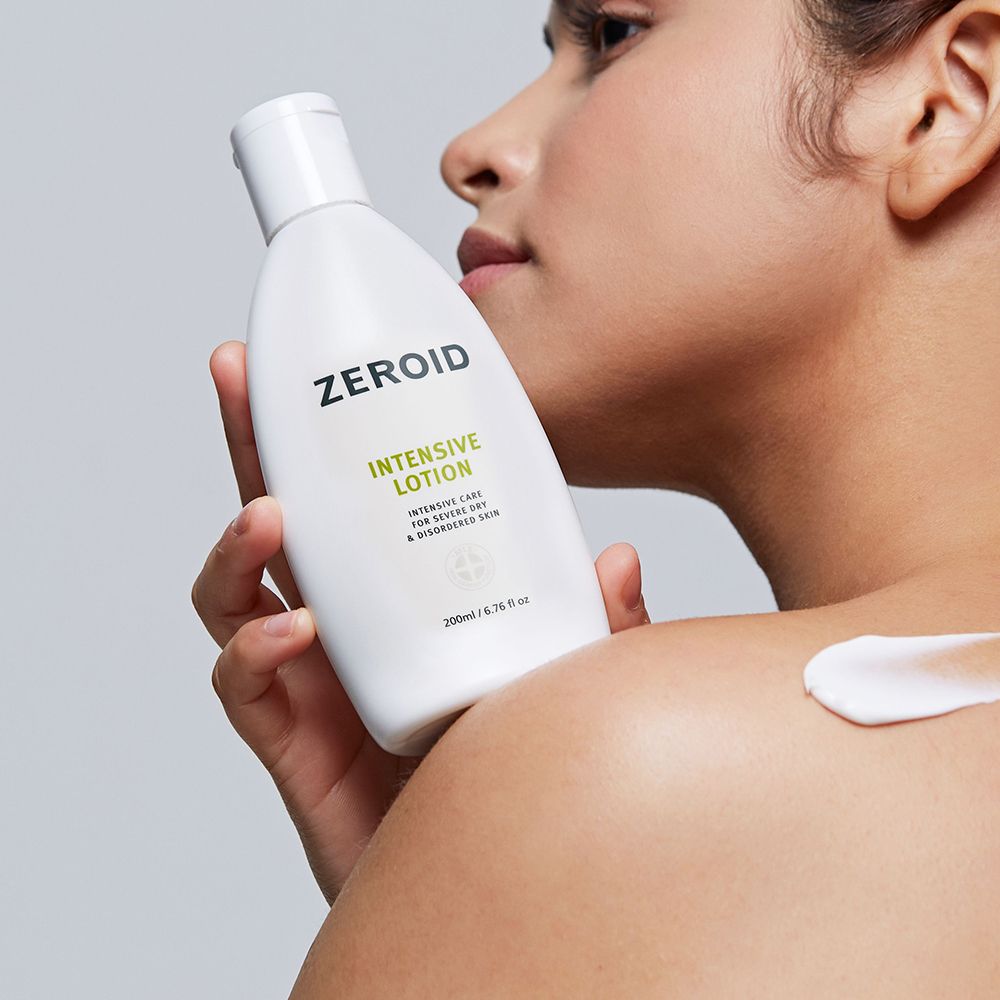 Persona che tiene in mano un flacone di ZEROID Intensive Lotion. Crema applicata sulla spalla. Testo verde.