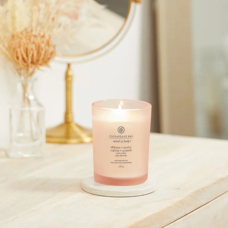Candela Chesapeake Bay accesa, mind & body, stillness + purity, 250g. Su sottobicchiere bianco, specchio sullo sfondo.