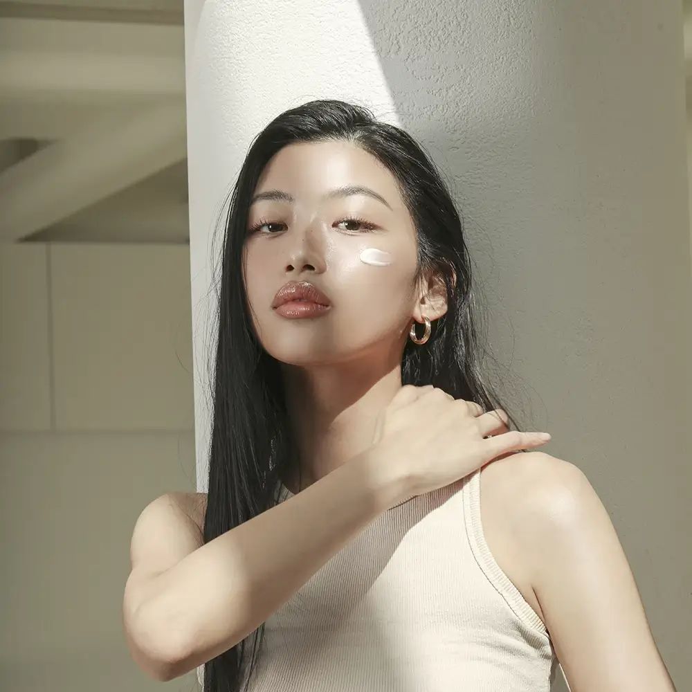 Donna con crema solare sulla pelle. Indossa una canotta e orecchini. Luce solare.