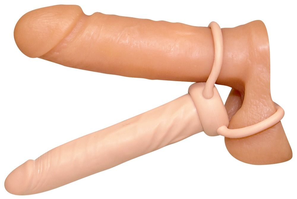 Due dildo beige con anello per pene e scroto. Uno è sopra l'altro. Gli anelli collegano i prodotti.