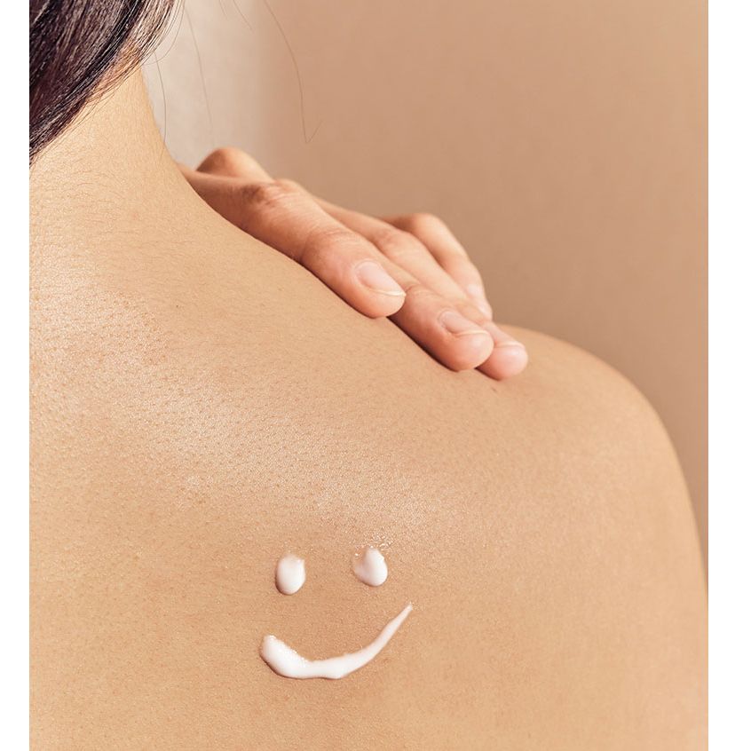 Primo piano di una zona della pelle con un sorriso fatto di crema. La pelle è chiara e liscia.