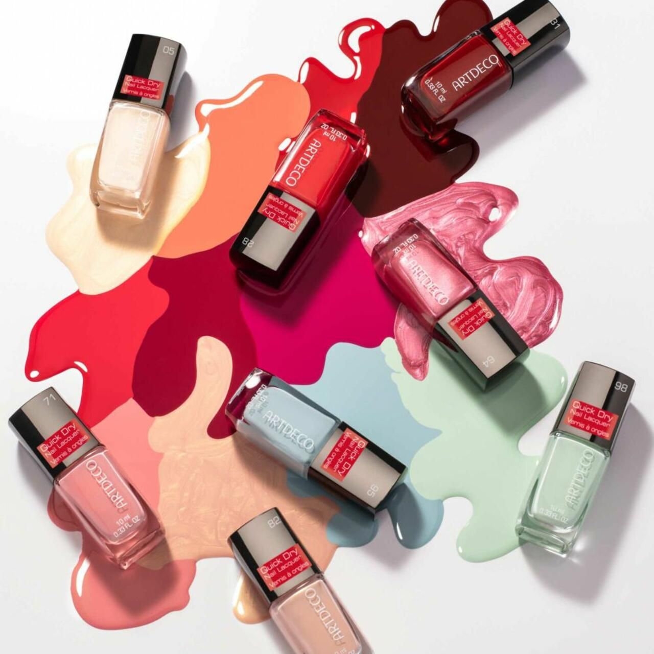 Diversi flaconi di smalto per unghie Artdeco Quick Dry su macchie di smalto colorate. Scritta: Quick Dry Nail Lacquer, Vernis à ongles.