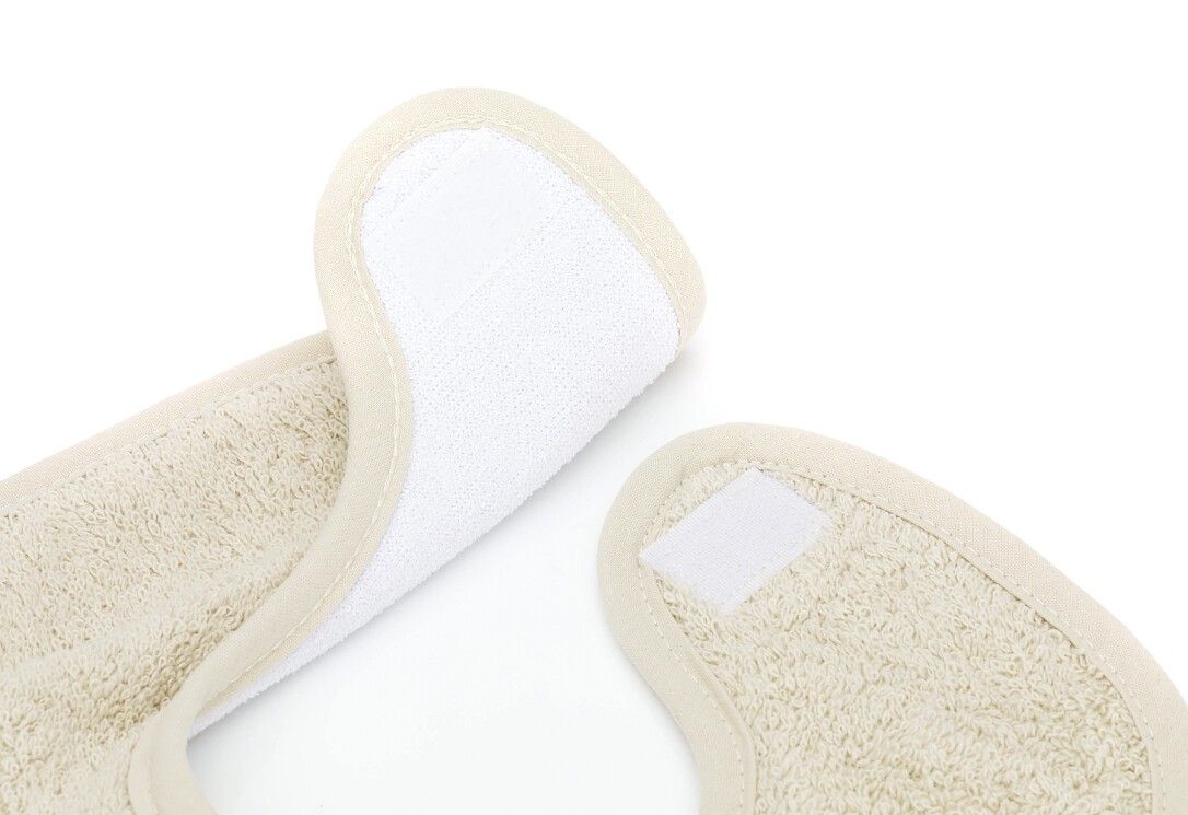 Primo piano dello scollo del bavaglino con chiusura in velcro. Materiale in spugna beige con bordo color crema.