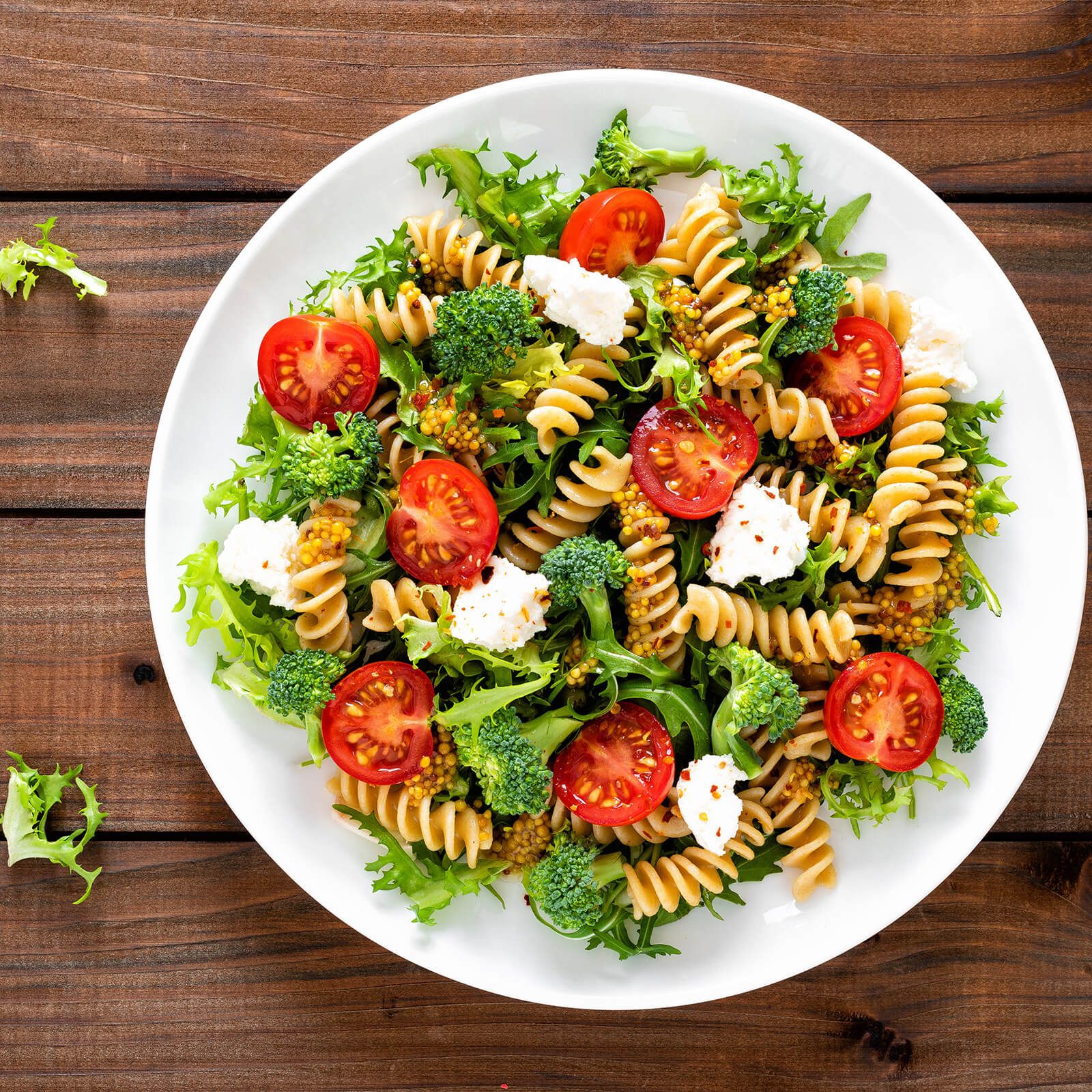 Piatto con insalata: fusilli, pomodori, broccoli, lattuga e formaggio. Su tavolo di legno.