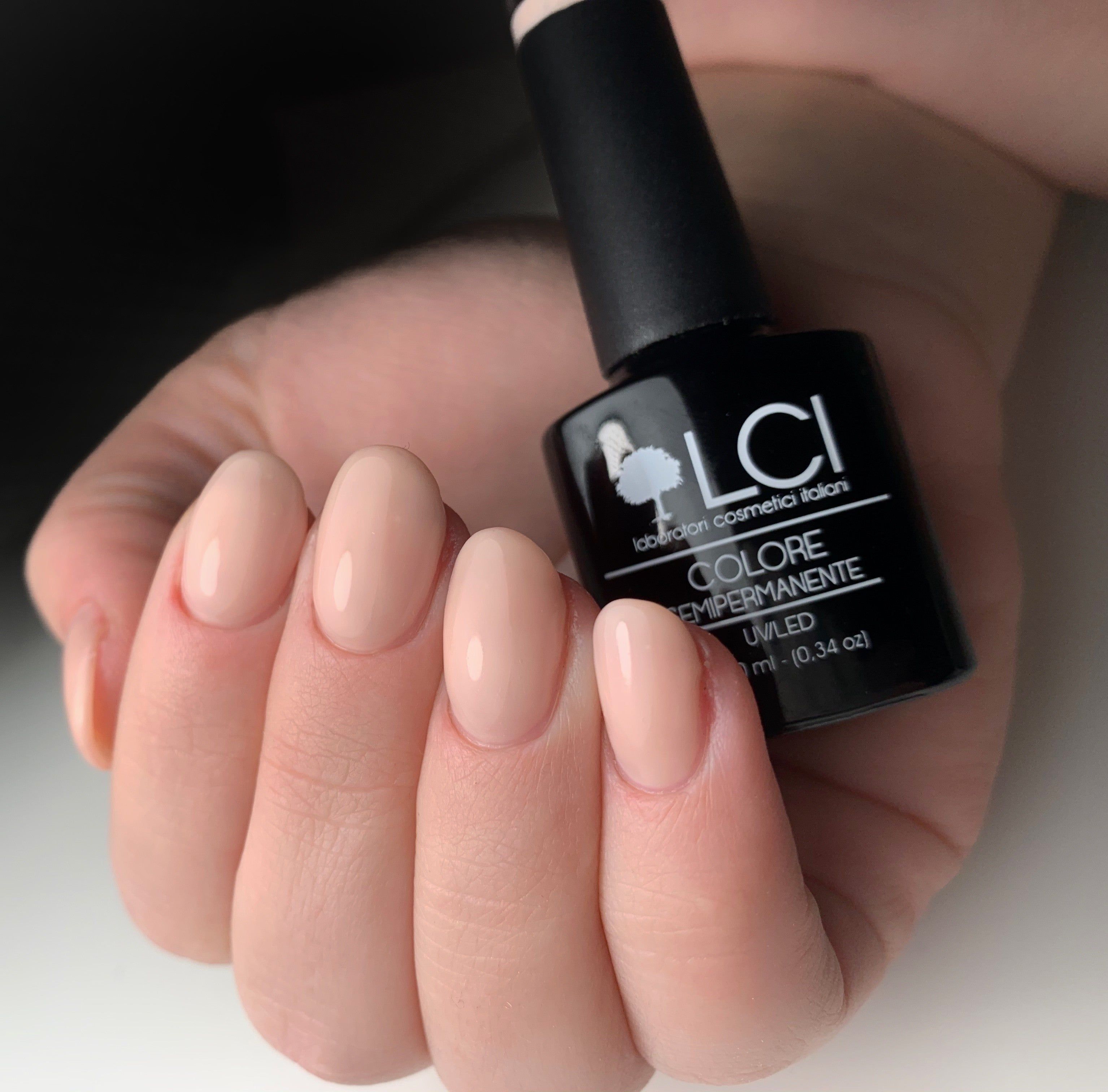 Mano con unghie smaltate rosa nude. Flacone di smalto accanto. Marchio LCI Cosmetics.