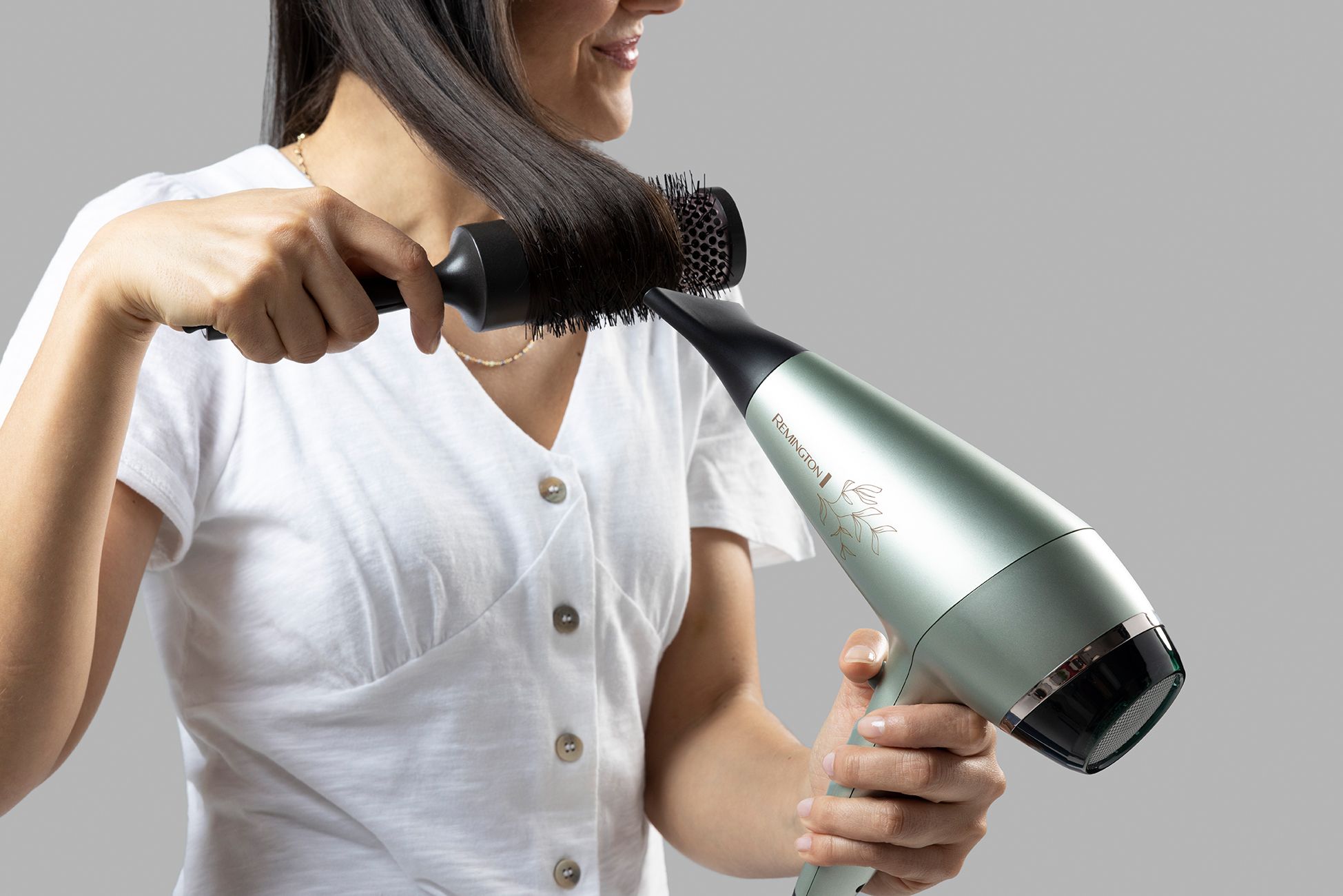 Una donna asciuga i suoi lunghi capelli scuri con un asciugacapelli Remington argentato.