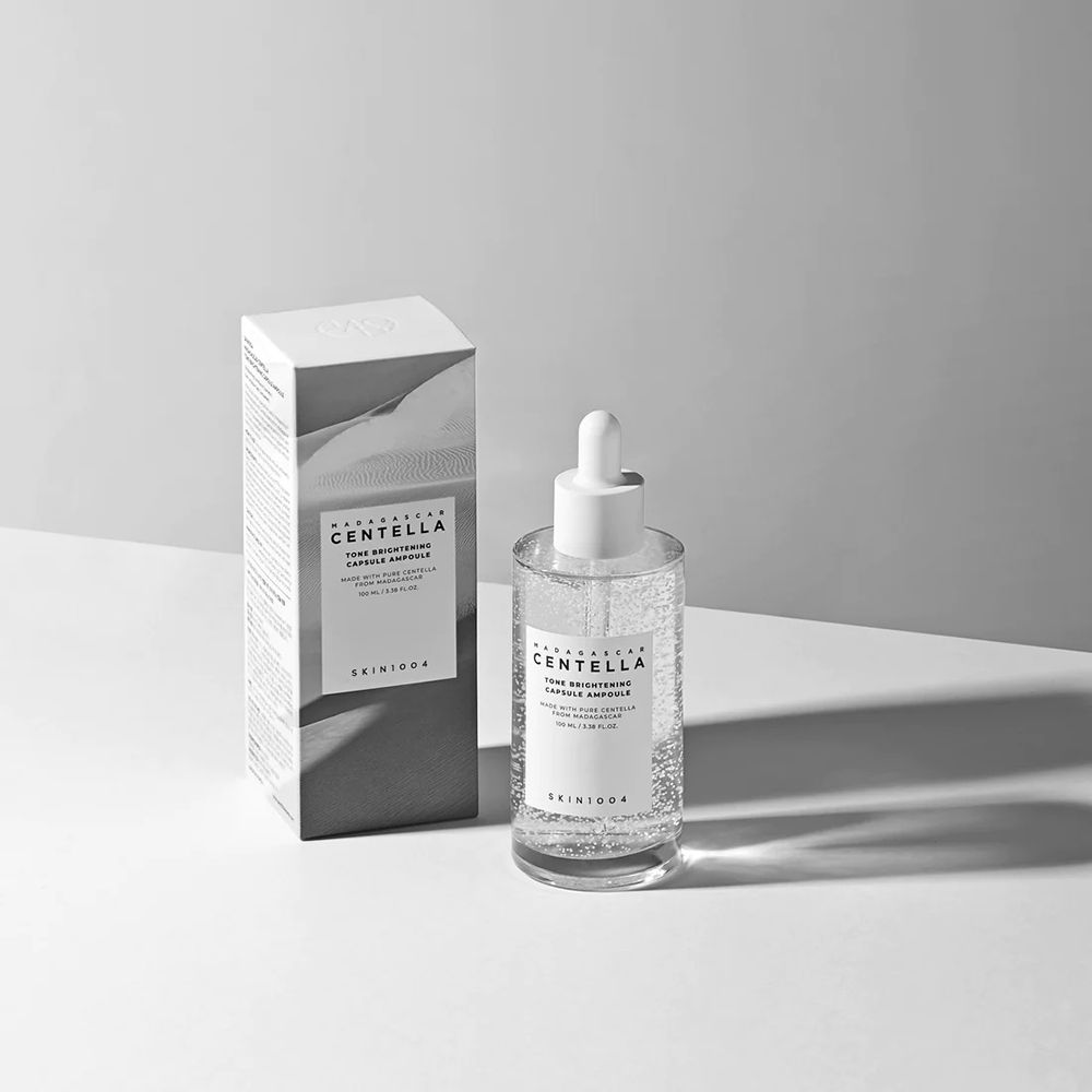 Flacone di siero e confezione. Flacone con etichetta bianca. Confezione con testo. Marchio: SKIN1004. Nome prodotto: Madagascar Centella Tone Brightening Ampoule.