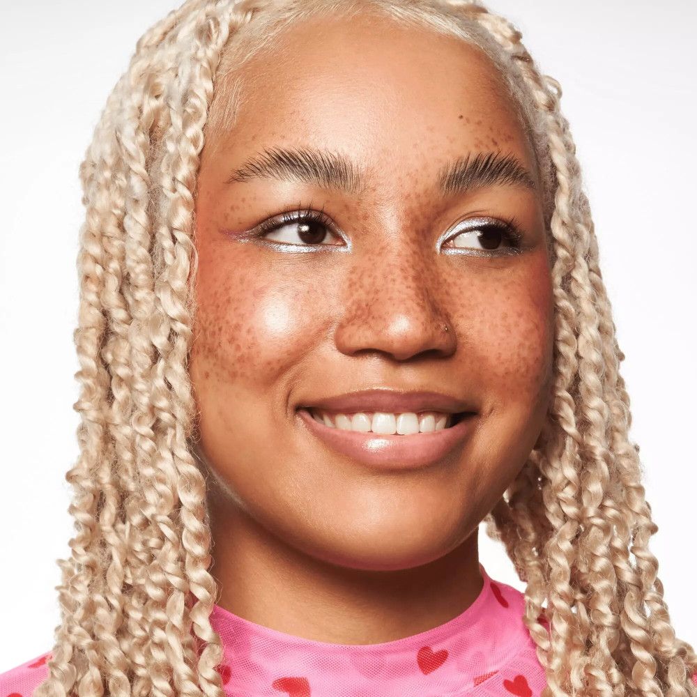 Ritratto di donna con trecce bionde. Indossa un top rosa. Il suo viso è truccato con fondotinta.