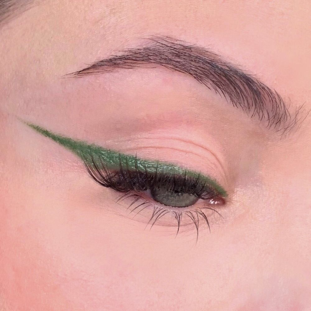 Eyeliner verde applicato su un occhio. Tratto preciso lungo la linea delle ciglia superiori. Sopracciglio visibile.