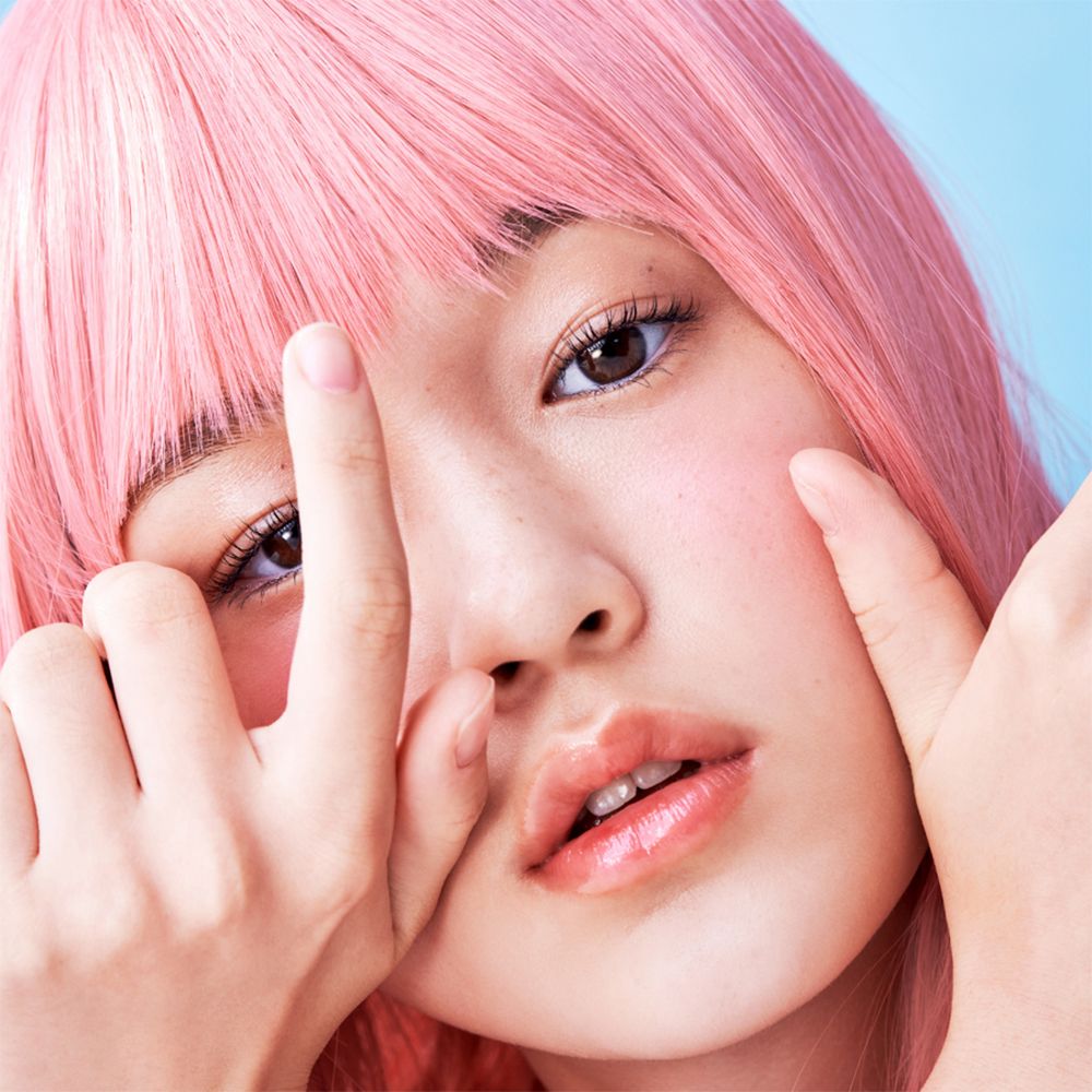 Ritratto di persona con capelli rosa che si tocca le labbra con le dita. Le labbra sono lucide.