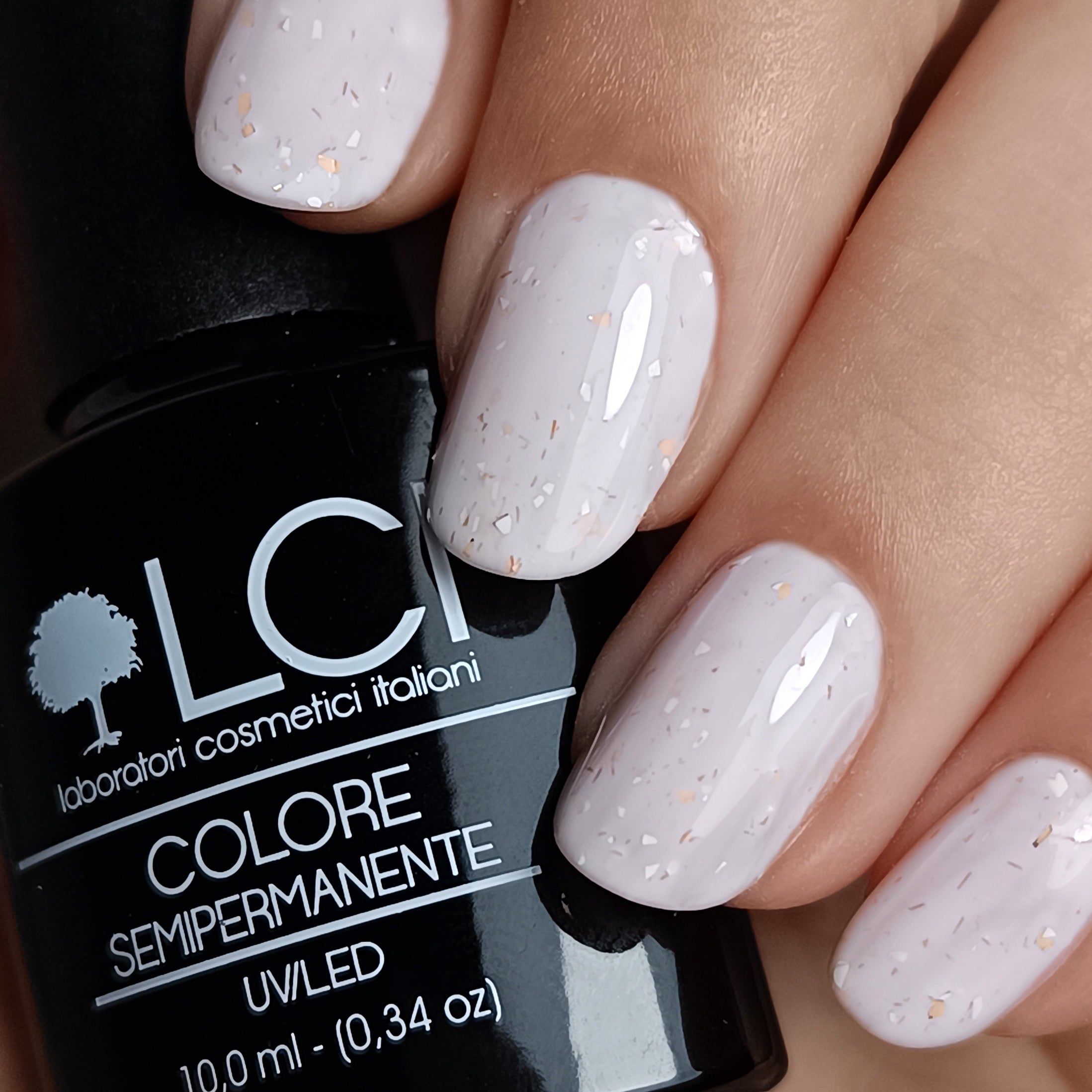 Primo piano di unghie smaltate e flacone di smalto. Unghie chiare con glitter. Flacone con tappo nero ed etichetta bianca.