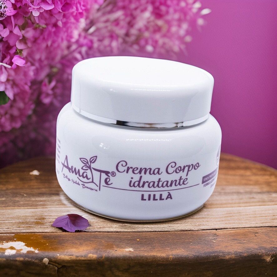 Vaso di crema bianco con coperchio. Scritta: Amatè Crema Corpo idratante Lillà. Su superficie in legno con fiori viola.