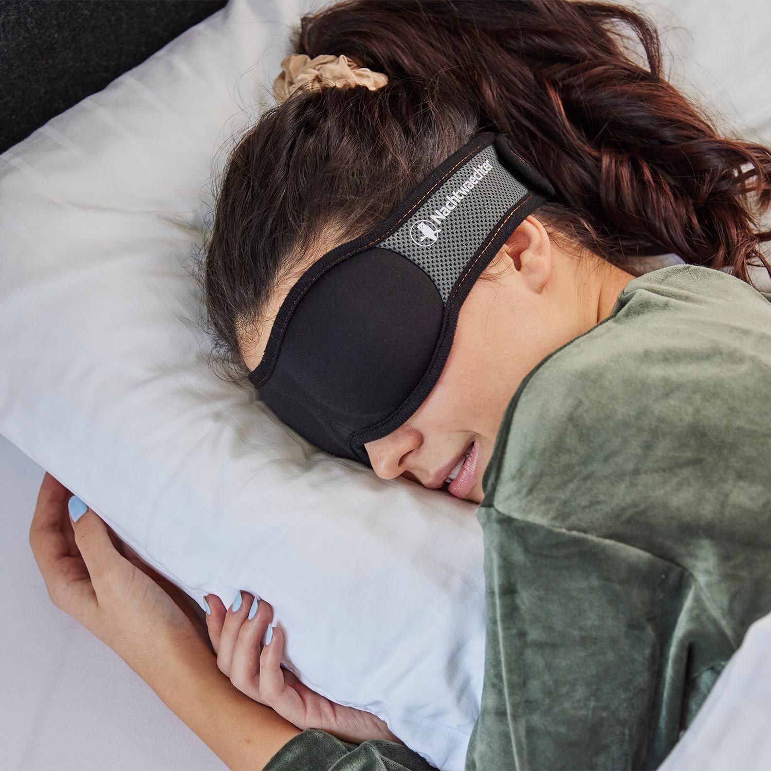 Donna con maschera per dormire nera a letto. Maschera sugli occhi, fascia grigia con logo.